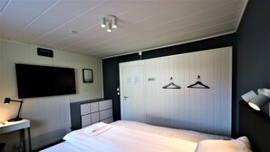 A hotel room with a bed, a desk with a lamp, a TV mounted on the wall, and a wardrobe with two hangers. - RIBO Apartment Arctic - Hostel (Kiruna)