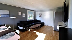 A modern living room with a black sofa, a wooden coffee table, a dining table with chairs, and a flat-screen TV mounted on the wall. - RIBO Apartment Arctic - Hostel (Kiruna)