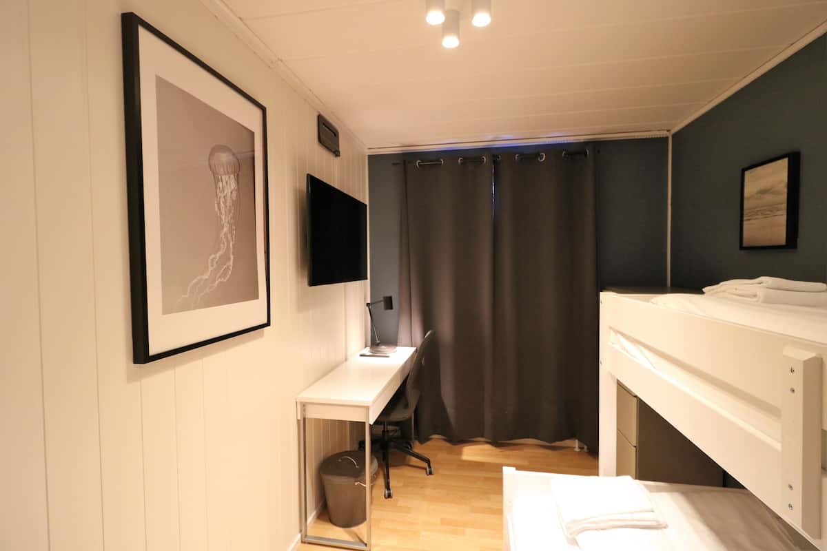 A bedroom with a bed, a desk with a chair, a TV, and a curtain.
