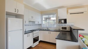 Kitchen features a refrigerator, stove, microwave, and sink, with a window and a small shelf for a coffee maker and toaster.