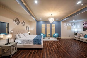A bedroom with a large bed, two blue armchairs, a small table, and a chandelier. - Best Location in Houston - Very spacious house - Close to everything (Houston)
