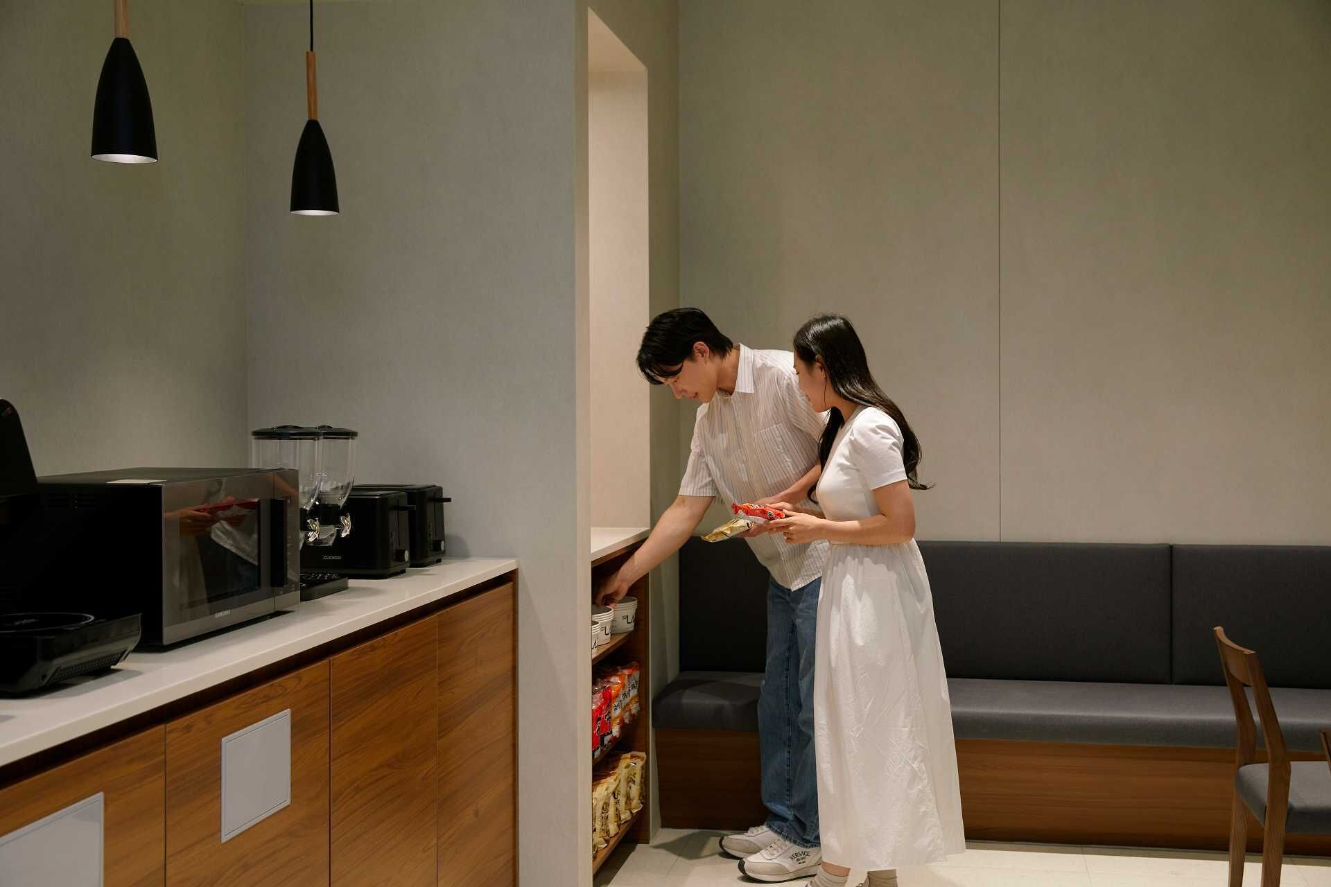 A modern kitchen with a microwave, toaster, and blender on the counter. There is a wooden cabinet below the counter and a grey sofa in the background.