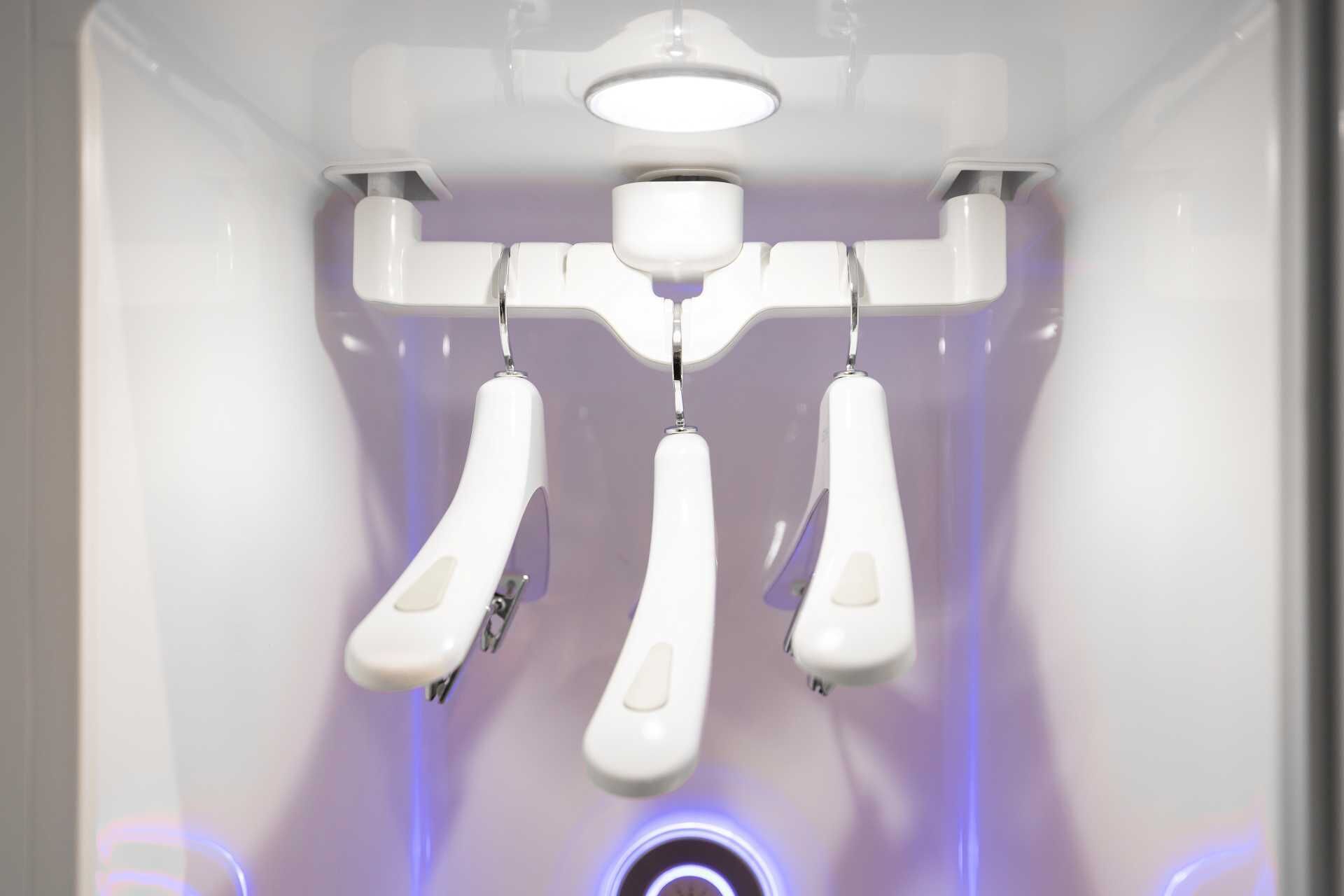 A ceiling-mounted, white, three-piece toilet fixture with a central control panel and a circular light below.