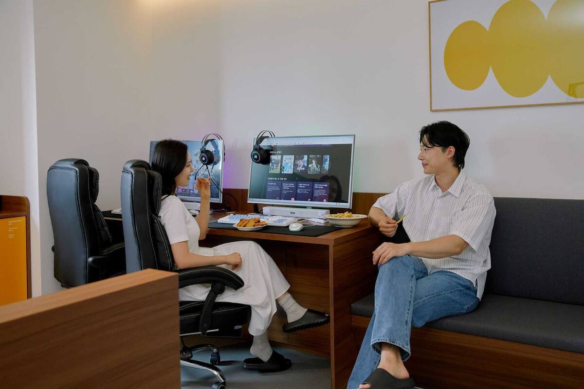 A room with a desk, two chairs, a computer, and a couch.