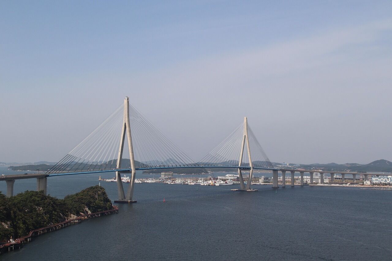 A cable-stayed bridge with two towers, a clear sky, and a marina in the background.