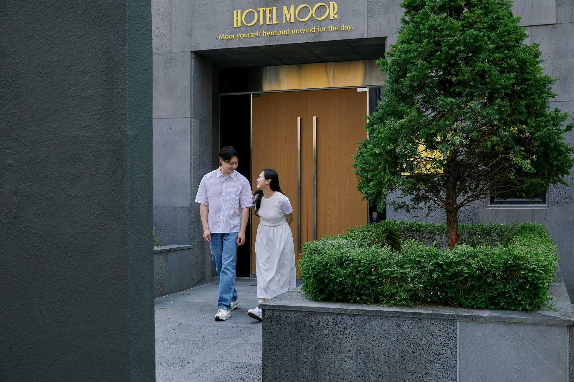 Entrada de un hotel con un letrero que dice "HOTEL MOOR" y una fachada de edificio moderna.
