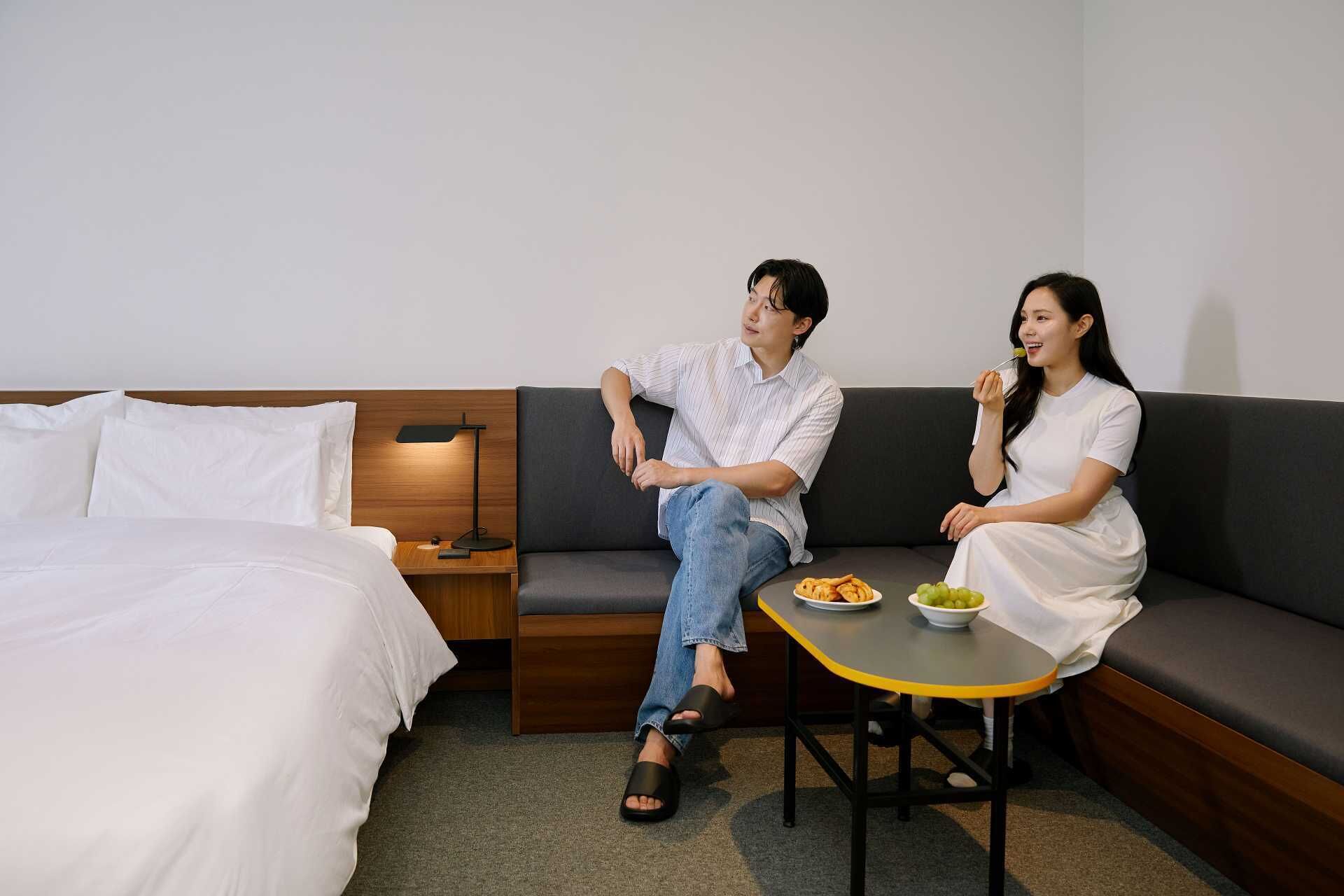 A modern hotel room with a bed, a sofa, a small table, and a nightstand.