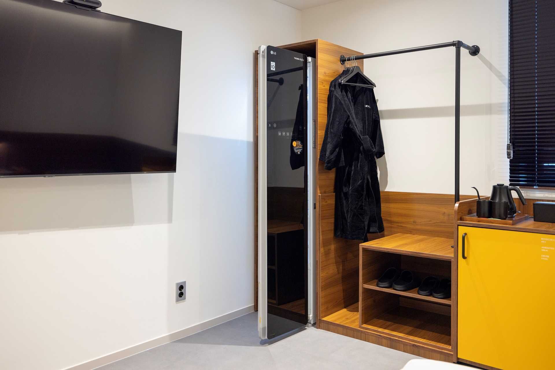A modern room with a sliding closet door, a TV mounted on the wall, a wooden shelf with shoes, and a yellow cabinet.