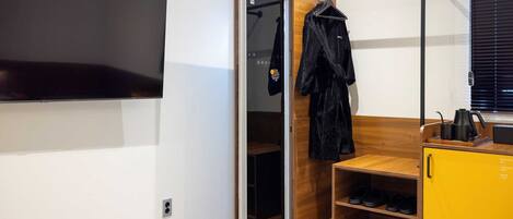 A modern room with a sliding closet door, a TV mounted on the wall, a wooden shelf with shoes, and a yellow cabinet.