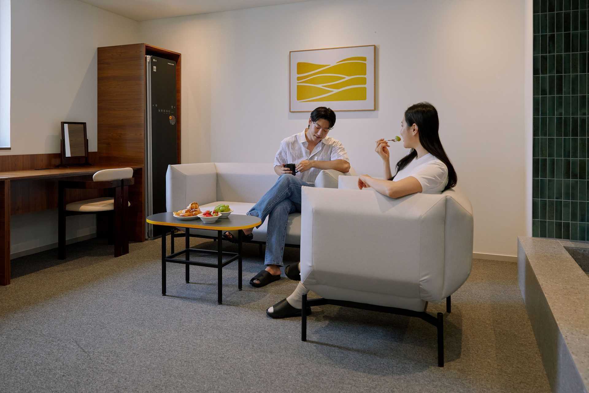 A modern hotel lobby with a wooden reception desk, a seating area with a small table, and a framed artwork on the wall.