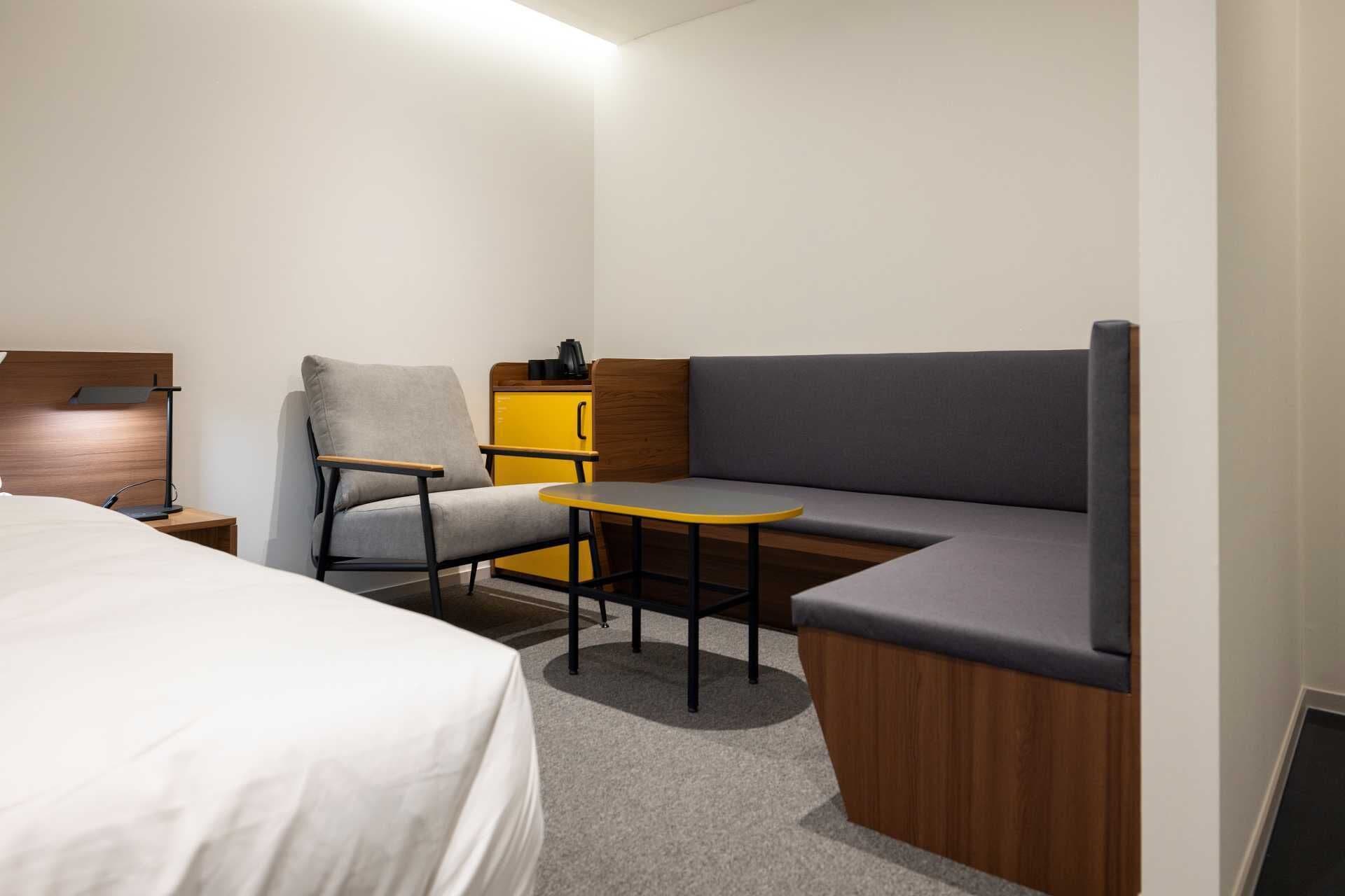 Una habitación de hotel compacta con cama, escritorio con silla, una mesita y un sofá.