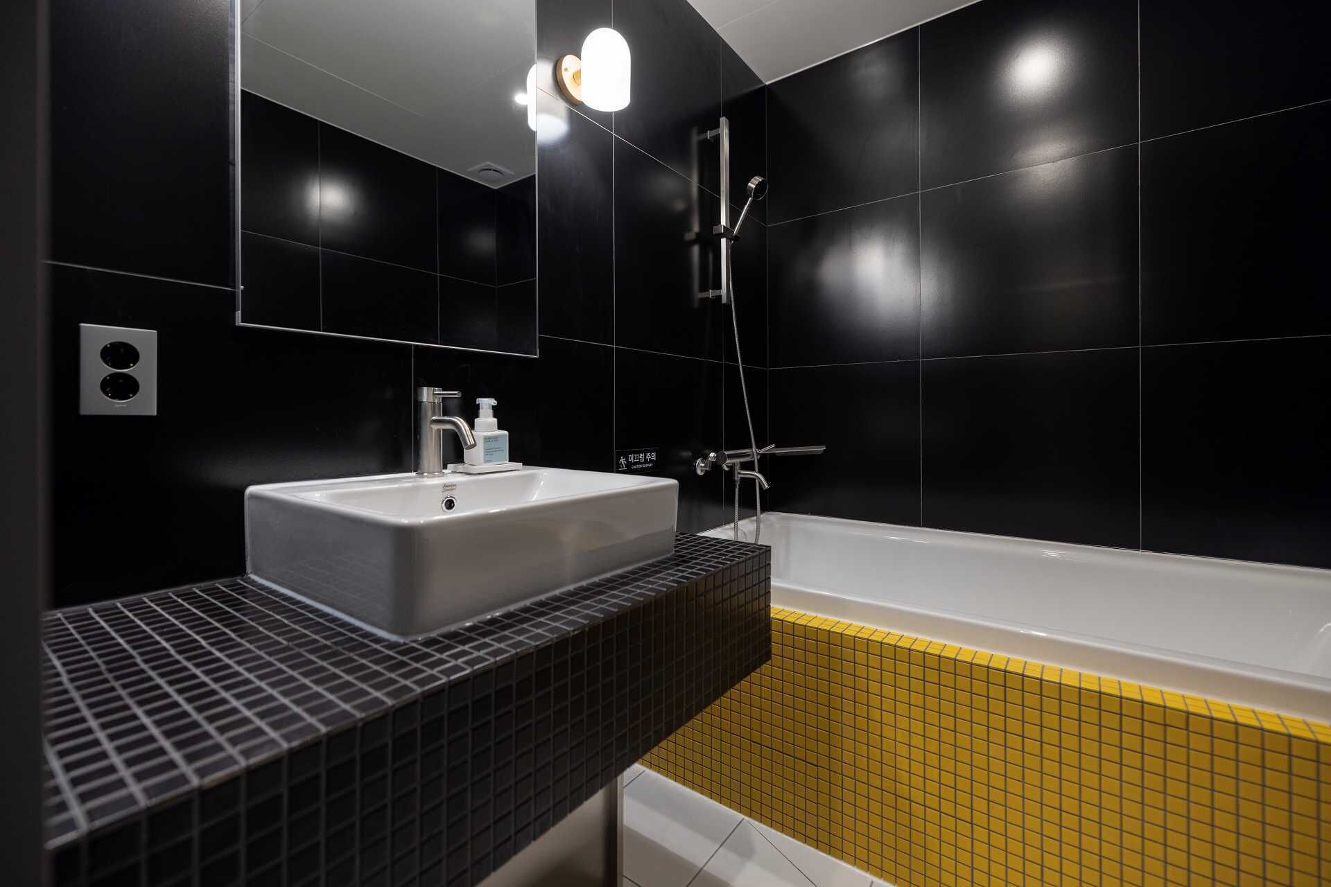 A modern bathroom with a white sink, black and yellow tiled walls, and a bathtub.