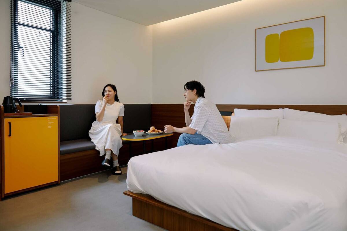 A hotel room with a bed, a sofa, a small table with food, and a kitchenette.