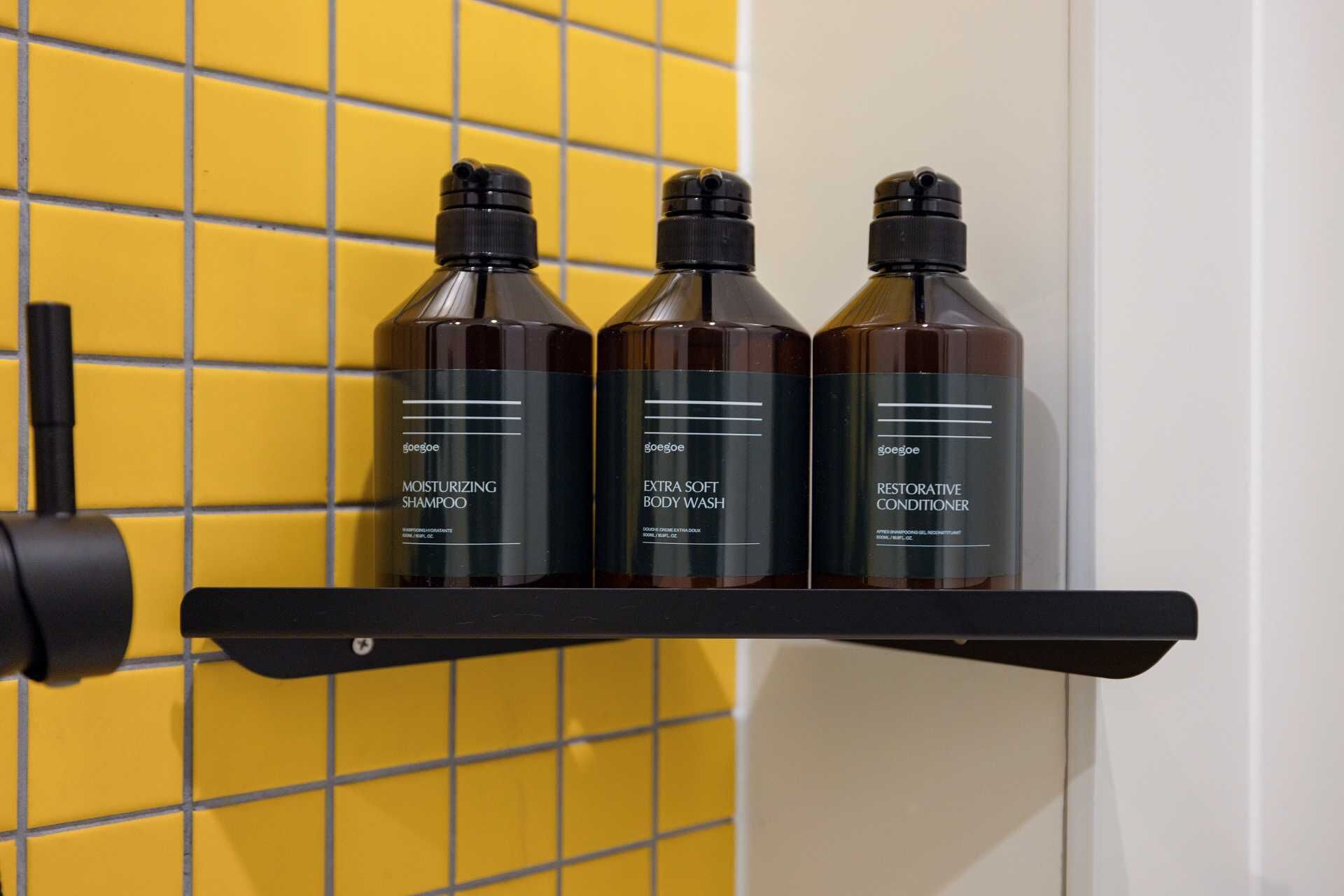 Une étagère avec trois bouteilles de produits de soins capillaires GoSoo, le tout placé devant un mur recouvert de carreaux jaunes.