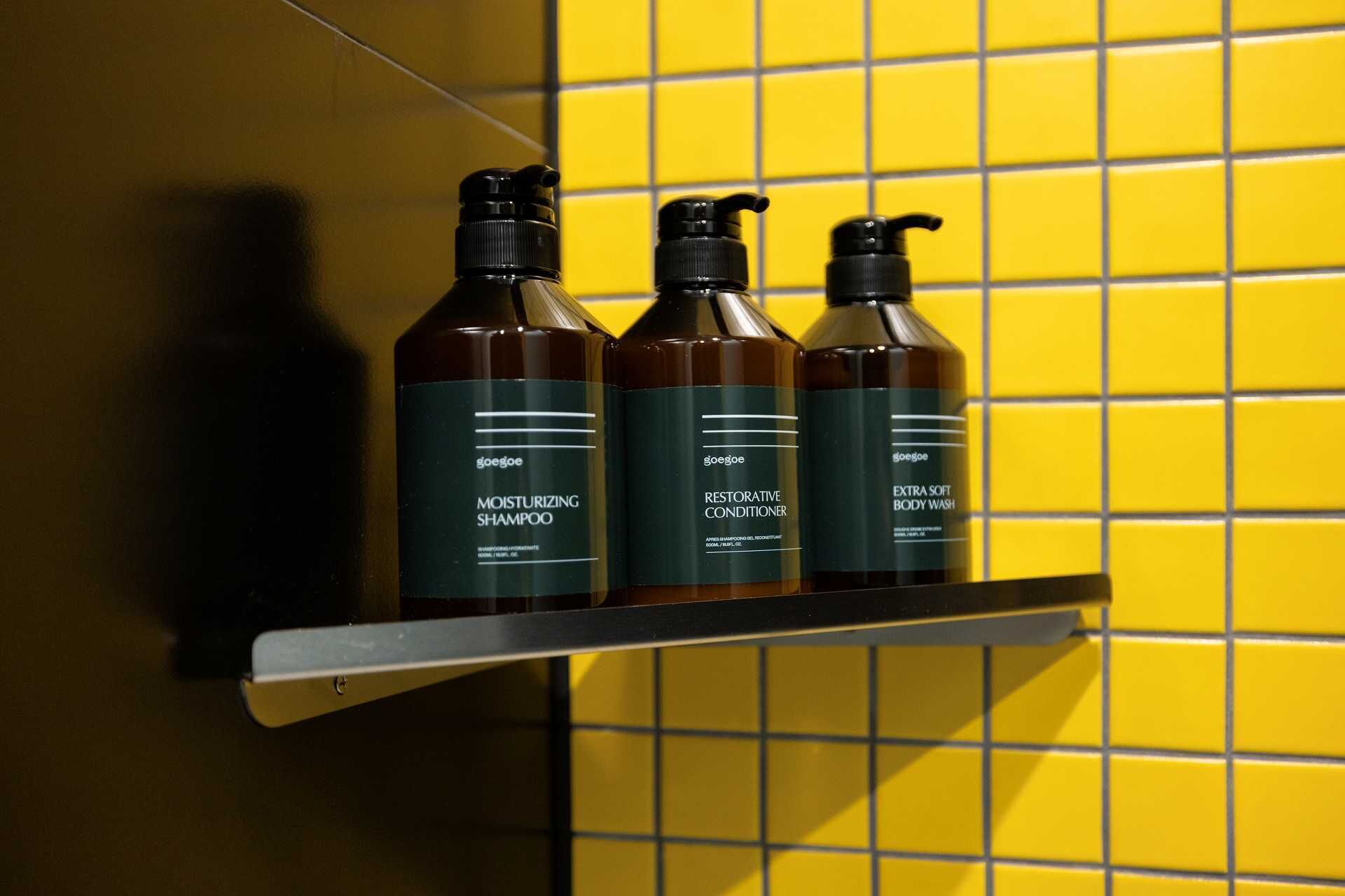 Three bottles of hair care products on a shelf against a yellow tiled wall.