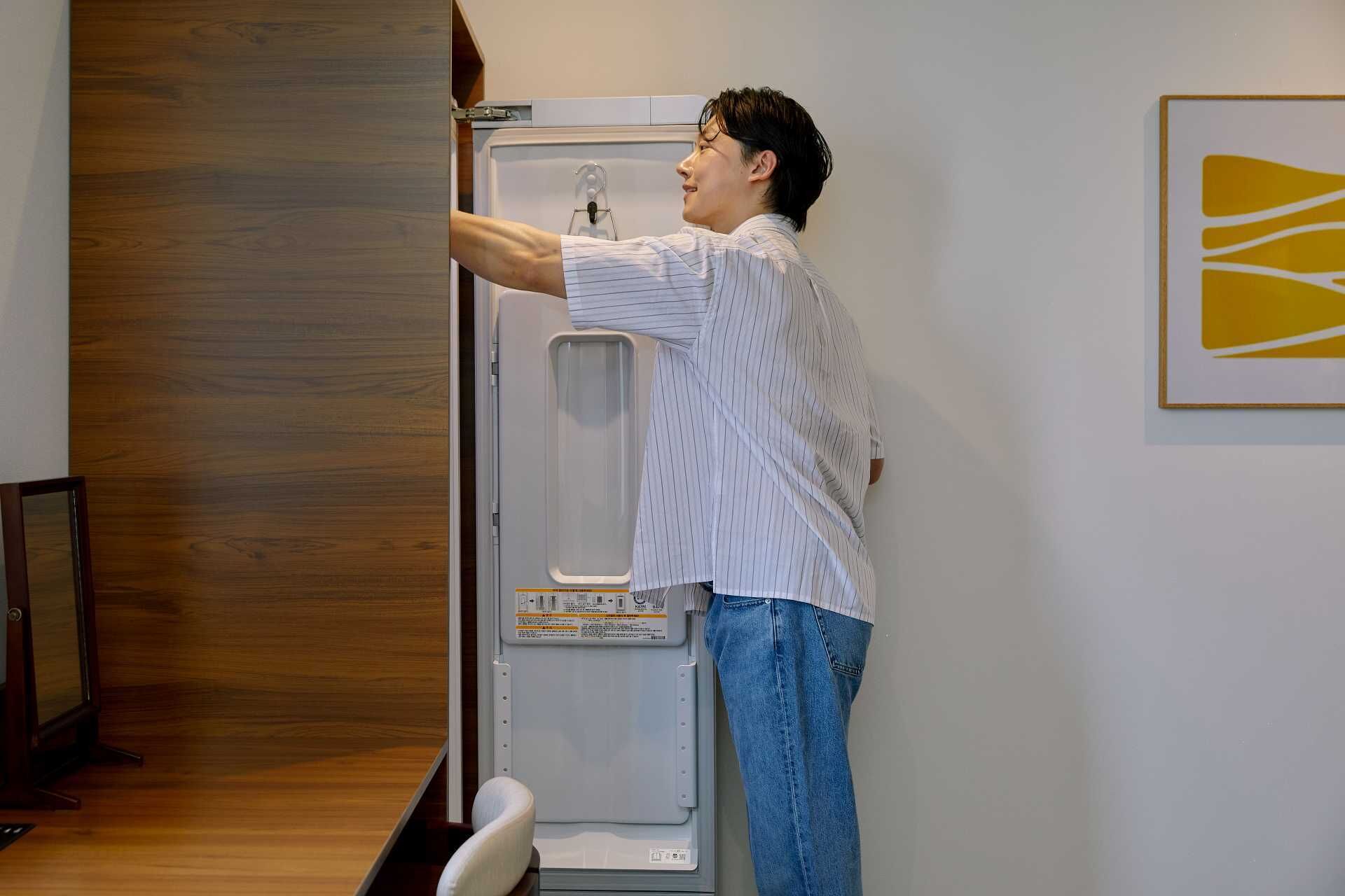 Una persona abriendo una puerta a un cuarto con piso de madera y pared blanca.