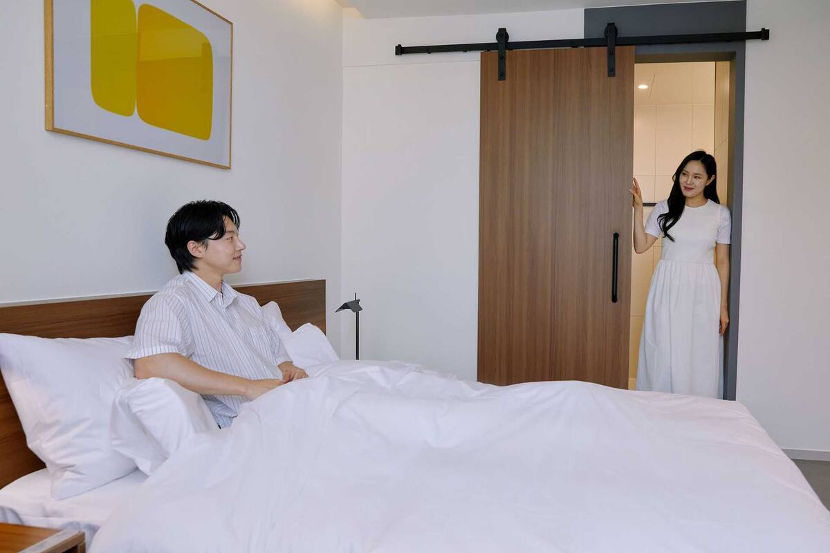 A hotel room with a bed, a wooden wardrobe, and a painting on the wall.