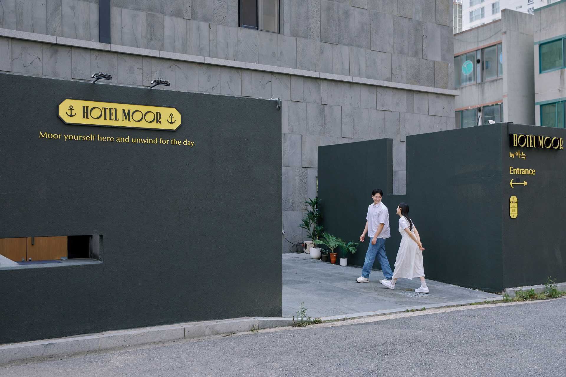 A modern building with a sign reading "HOTEL MOOR" and a tagline "Moor yourself here and unwind for the day."