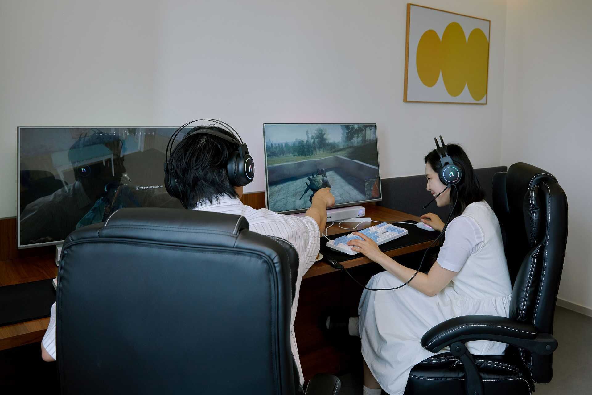 Dos personas sentadas en un escritorio con un monitor de computadora, teclado y ratón.