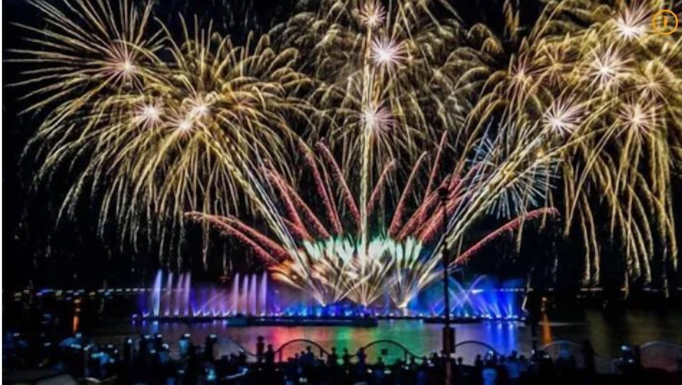 A nighttime fireworks display over a body of water with a crowd of people watching.
