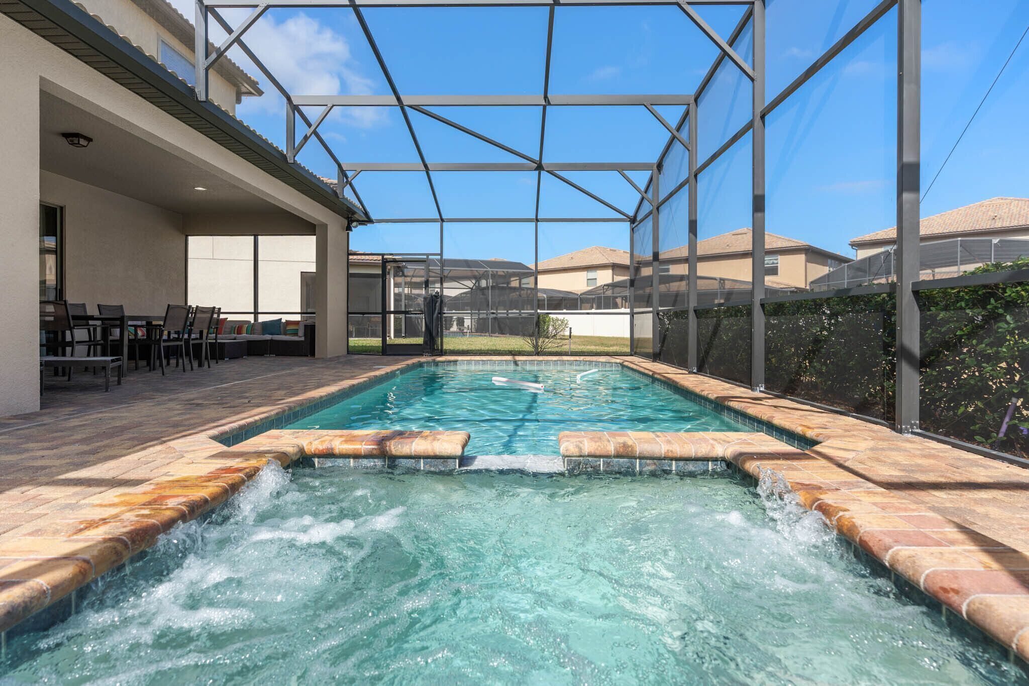 A swimming pool with a hot tub, surrounded by a covered patio area with chairs and tables.