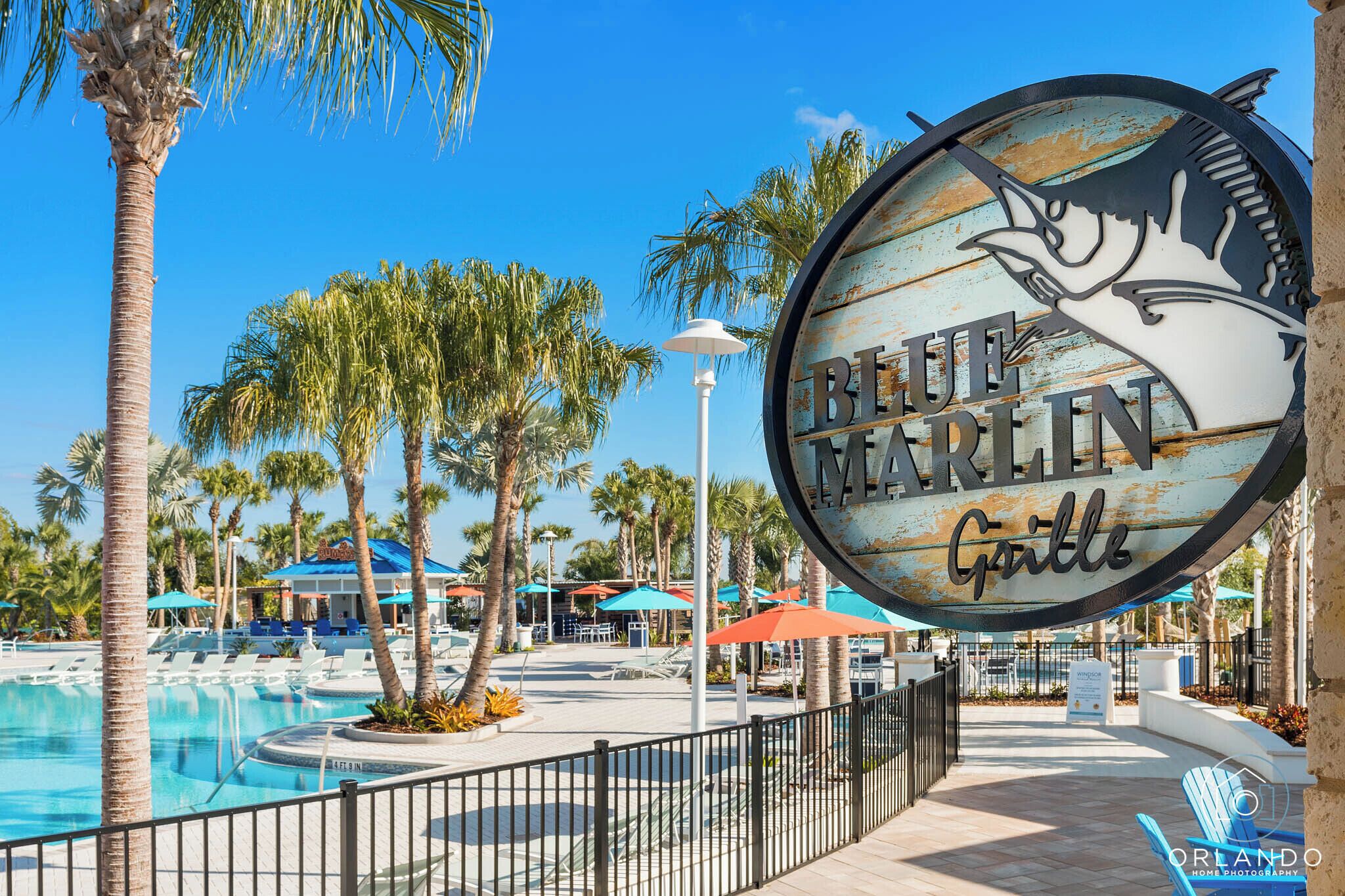 A pool area with lounge chairs and umbrellas, a sign for 'Blue Marlin Grill', and palm trees.