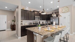 A modern kitchen with dark cabinets, granite countertops, a central island with bar stools, stainless steel appliances, and pendant lighting.