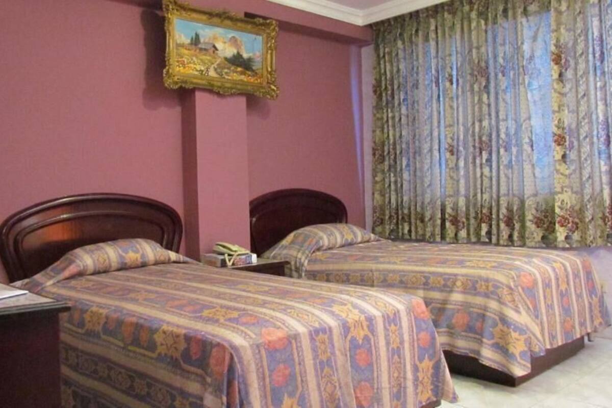 A room with two single beds, a desk with a chair, a telephone, and a framed picture on the wall.