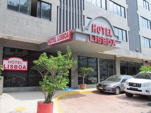 Een hotel genaamd "Hotel Lisboa" met een moderne gevel, een overdekte ingang en een parkeerplaats met auto's.