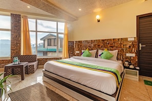 A hotel room with a large bed, a view of a mountain, and a stone wall. - Treebo Srishti Vaikunth With Mountain View (Shimla)