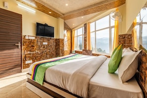 A bedroom with a stone wall, a bed with a colorful blanket, a flat-screen TV, and a window with curtains. - Treebo Srishti Vaikunth With Mountain View (Shimla)