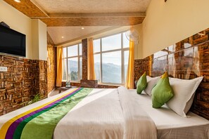 Una habitación de hotel con una cama grande, un televisor montado en la pared y vistas a las montañas a través de las ventanas.