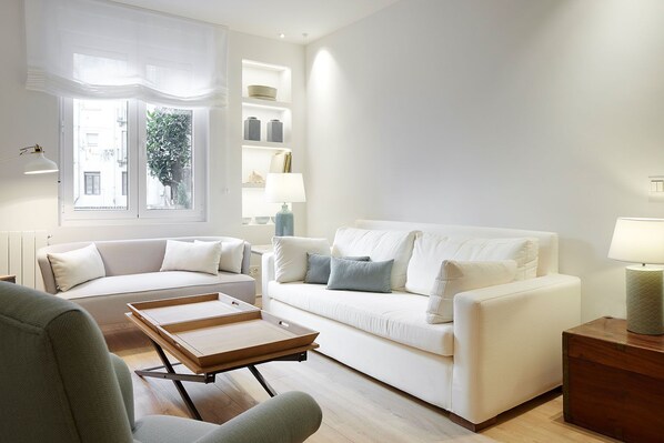 Ein modernes Wohnzimmer mit einem weißen Sofa, einem Holztisch und Blick auf eine Stadtlandschaft durch ein großes Fenster.