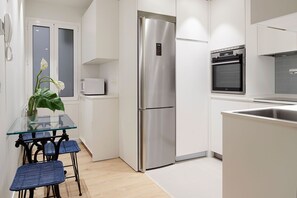 Eine moderne Küche mit einem Edelstahl-Kühlschrank, einem eingebauten Backofen und einem Esstisch mit Glasplatte sowie blauen Stühlen.