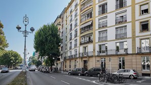Un immeuble à plusieurs étages doté de balcons, avec des voitures garées et des vélos sur le trottoir.