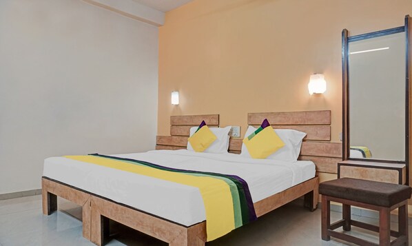 A hotel room with a wooden bed frame, white bedding, a bench, and a mirror.