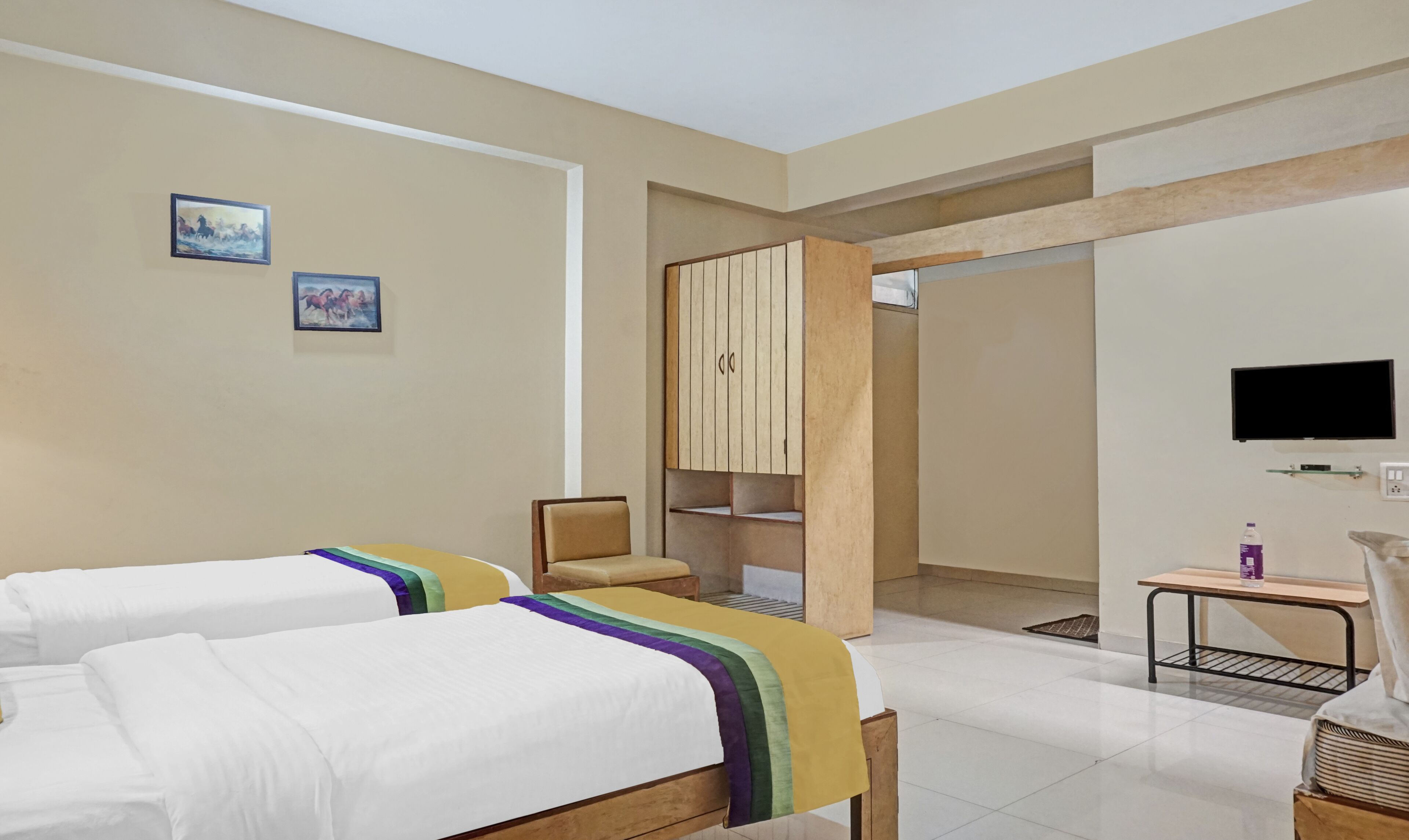 A hotel room with two beds, a TV, a small table, and a wardrobe.
