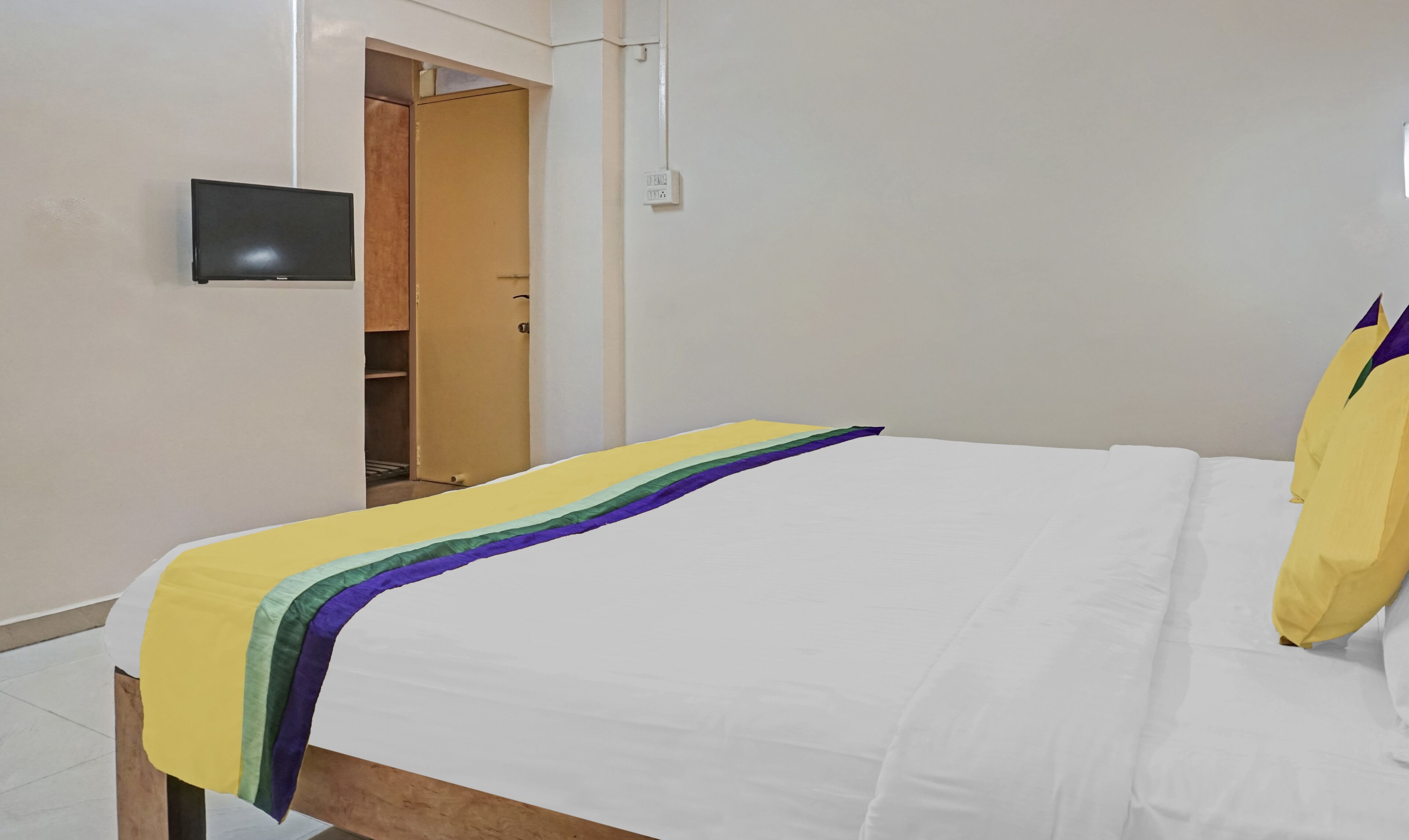 Une chambre d’hôtel avec un lit, un téléviseur fixé au mur et une porte donnant sur un placard.