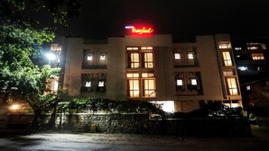 A hotel with a prominent red sign, multiple windows, and a stone wall in front.