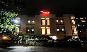 A hotel with a prominent red sign, multiple windows, and a stone wall in front.