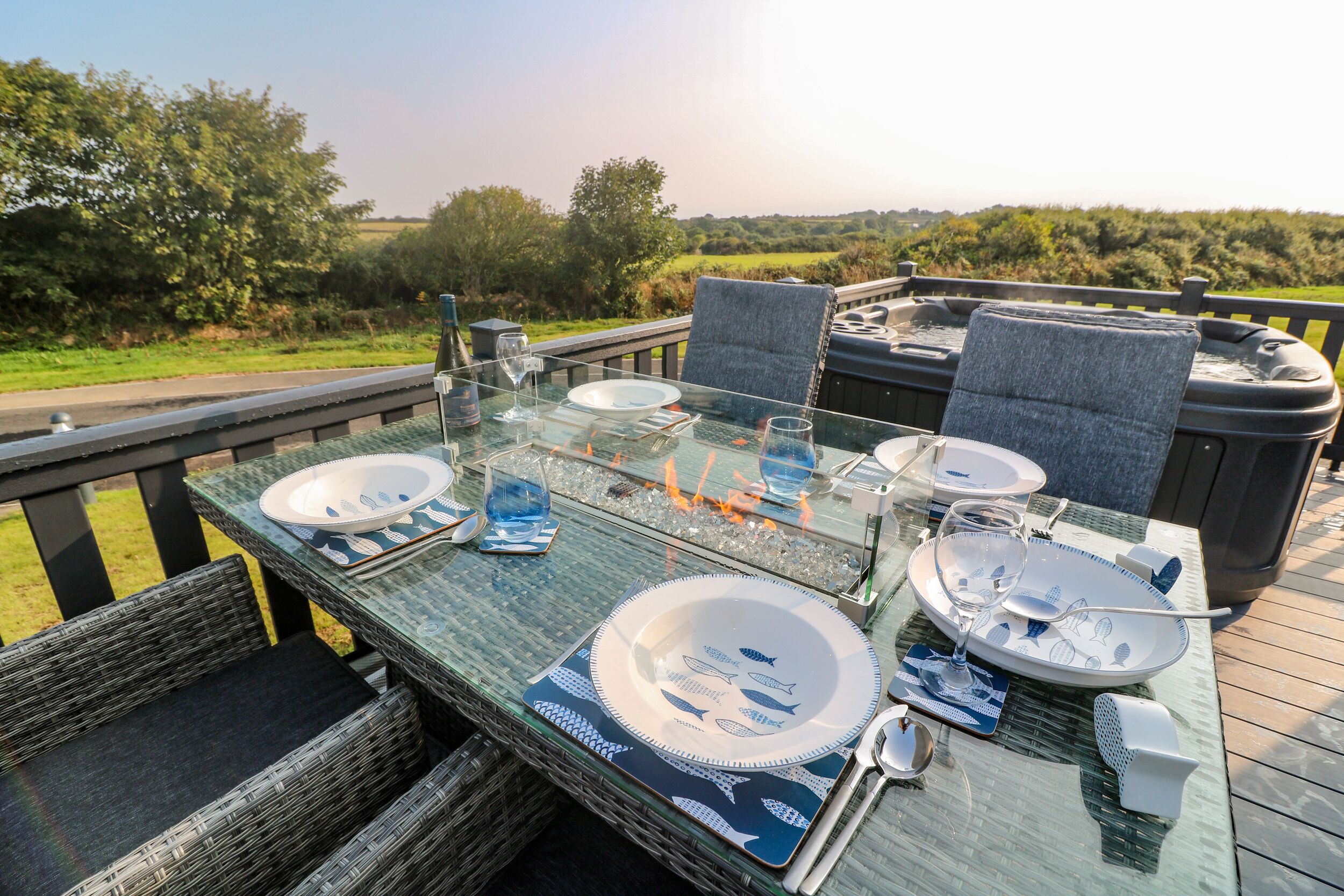 An outdoor dining area with glass tables, wicker chairs, and a view of the countryside.