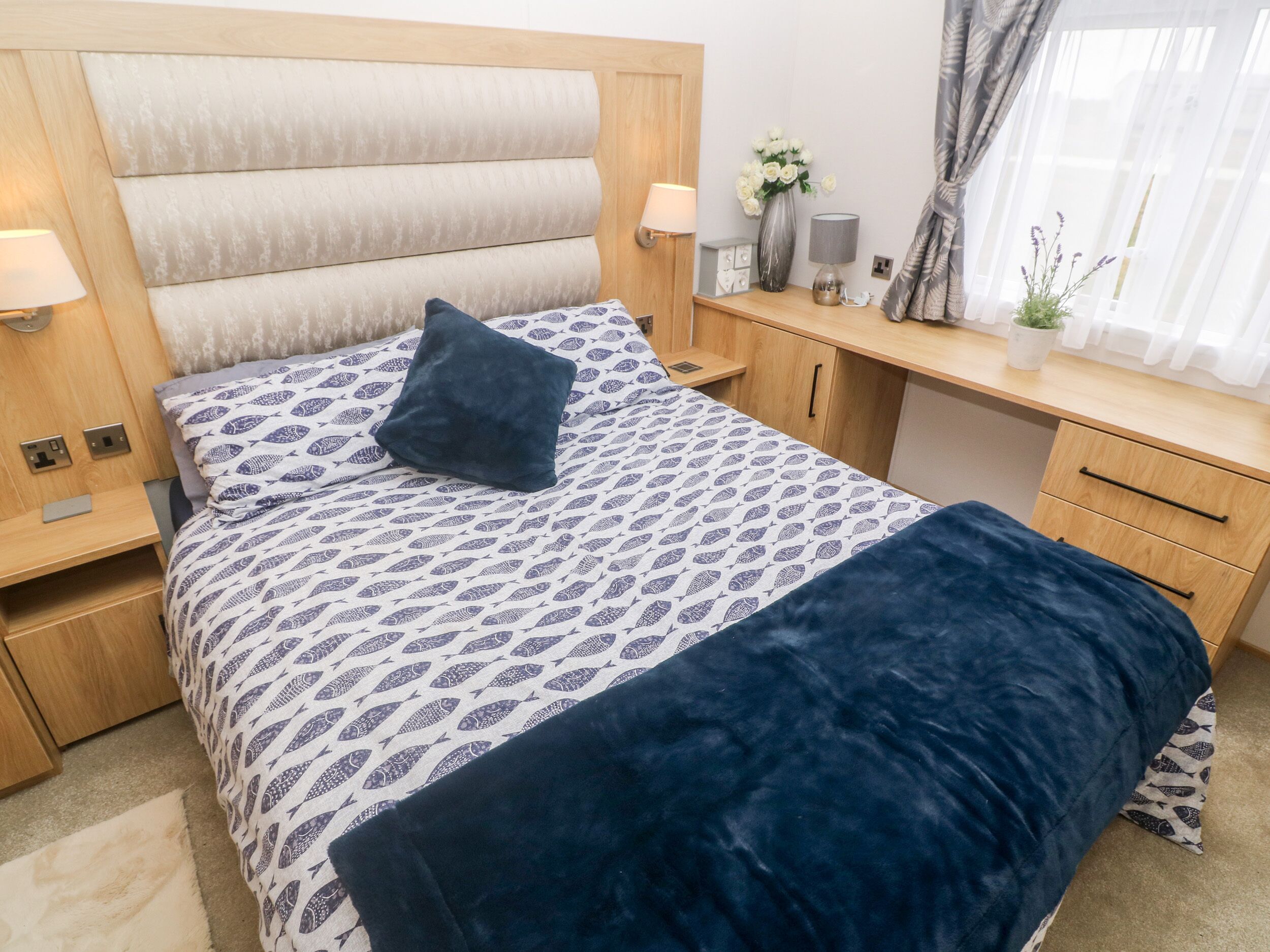 Ein ordentlich eingerichtetes Schlafzimmer mit einem Bett, Nachttischen, einem Schreibtisch und einem Fenster mit Vorhängen.