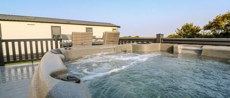 A hot tub area with a wooden deck, a building in the background, and a clear sky.