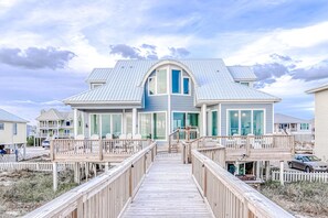 Ett stort hus med en inglasad veranda och ett trädäck som leder fram till entrén.