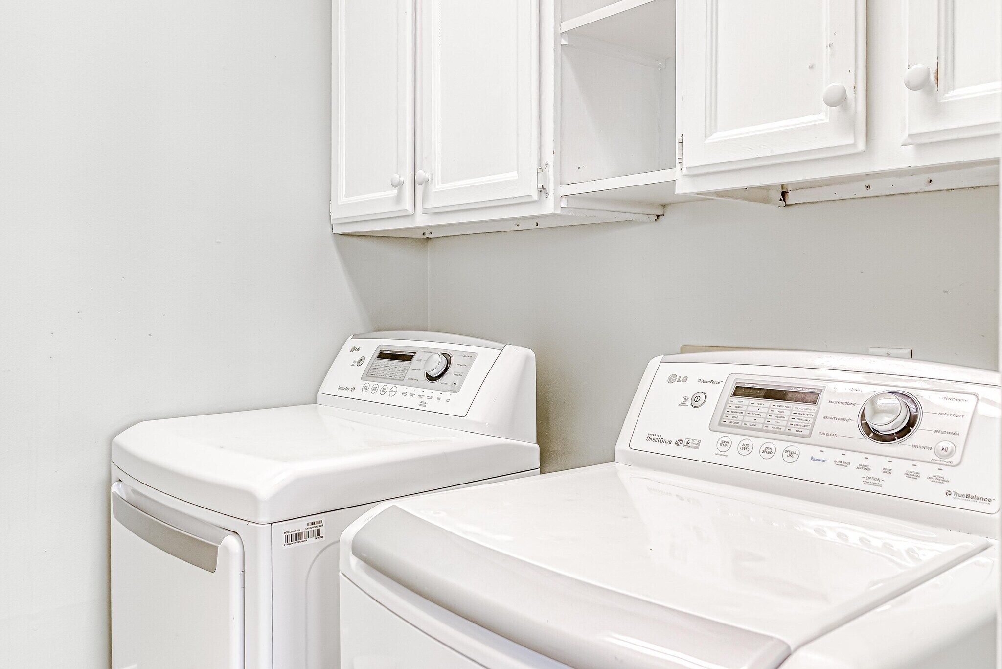 Two white front-loading washing machines in a laundry room with white cabinetry above.
