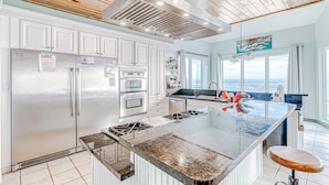 A modern kitchen with white cabinets, stainless steel appliances, and a large island with a granite countertop. - Beachfront in Morgantown (Gulf Shores)