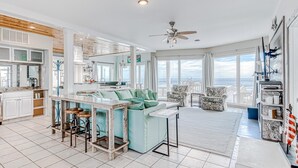A spacious living area with a kitchen, dining area, and large windows offering a view of the ocean. - Beachfront in Morgantown (Gulf Shores)