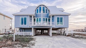 A two-story house with a balcony, a covered entryway, and a sandy driveway. - Beachfront in Morgantown (Gulf Shores)