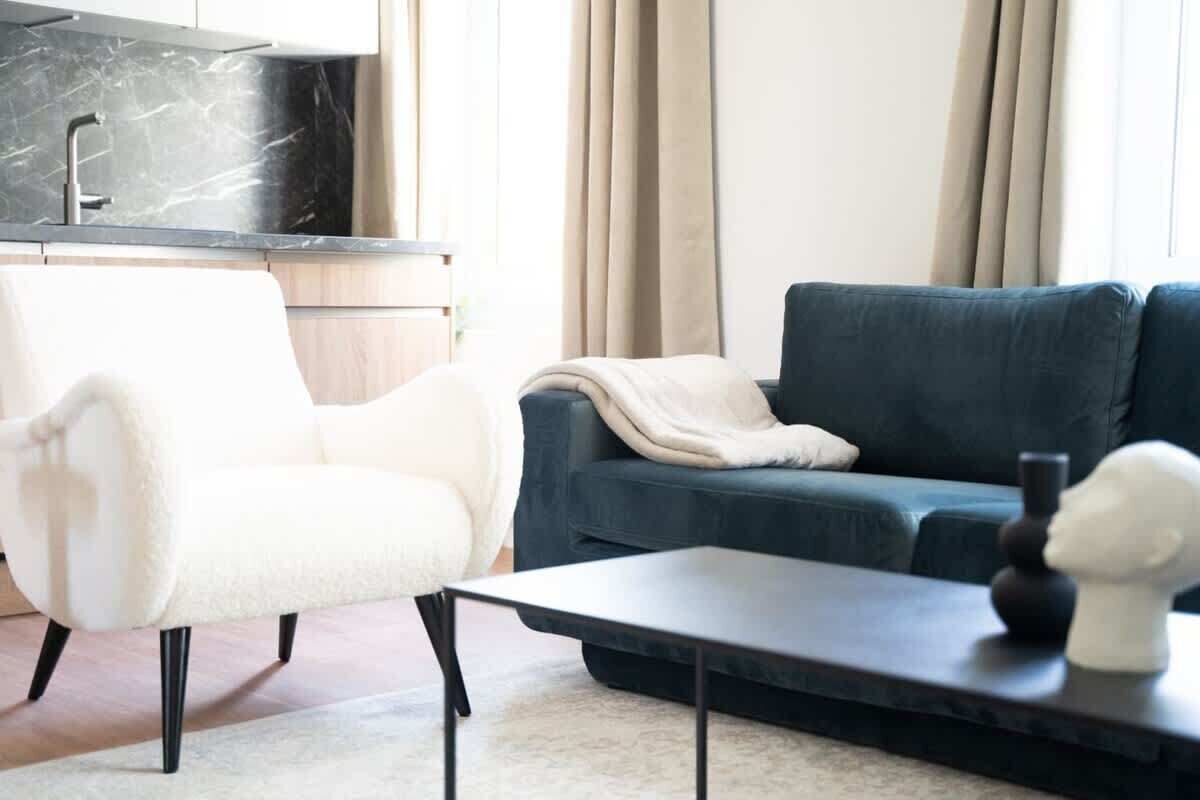A modern living room with a sofa, a chair, a coffee table, and a kitchen area with a marble countertop and sink.