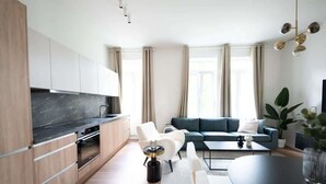Una cucina moderna con elettrodomestici integrati, un'area pranzo con tavolo nero e un soggiorno con divano e pianta.